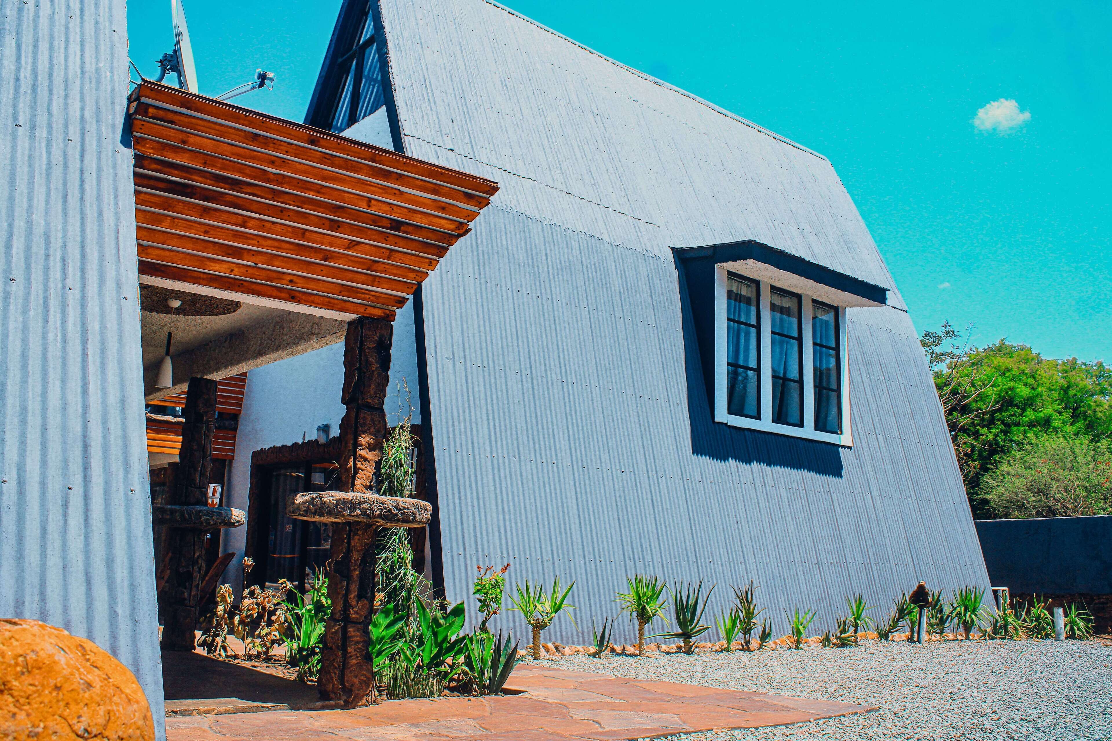 A modern building with a blue exterior, a wooden pergola, and a small window.