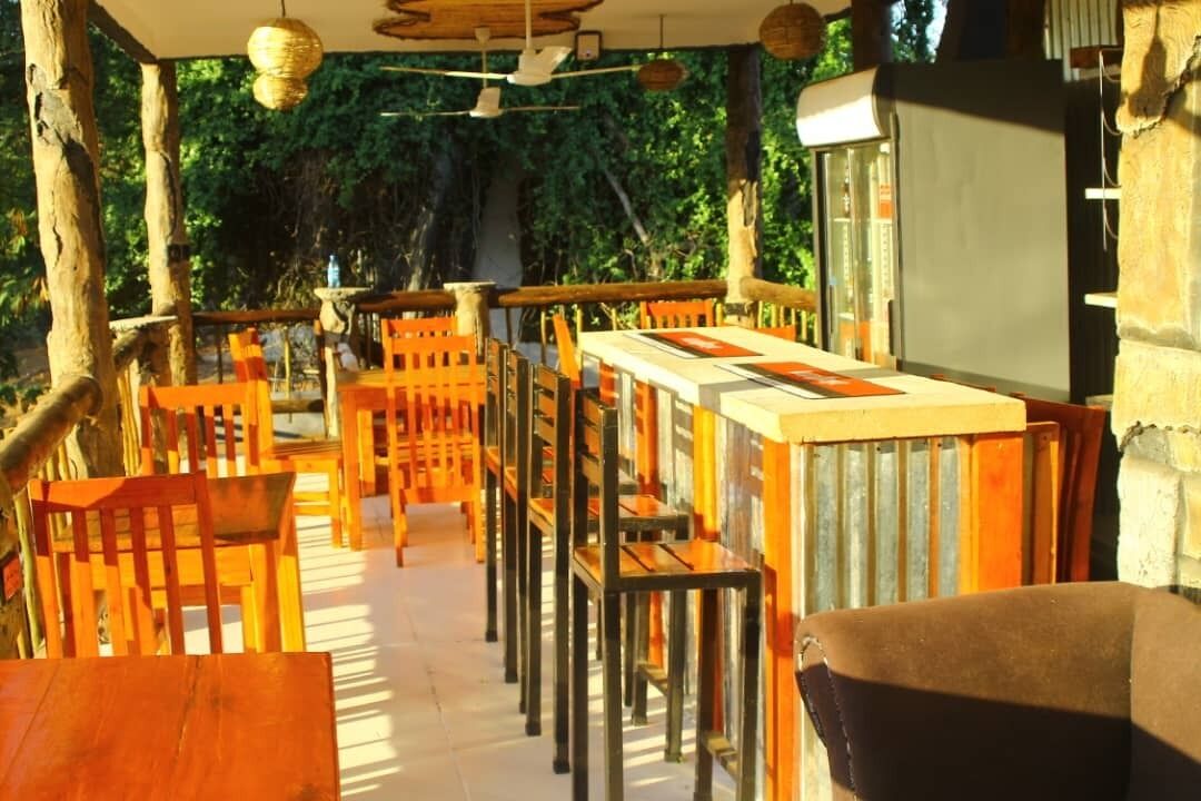 An outdoor restaurant with wooden tables and chairs, surrounded by trees.