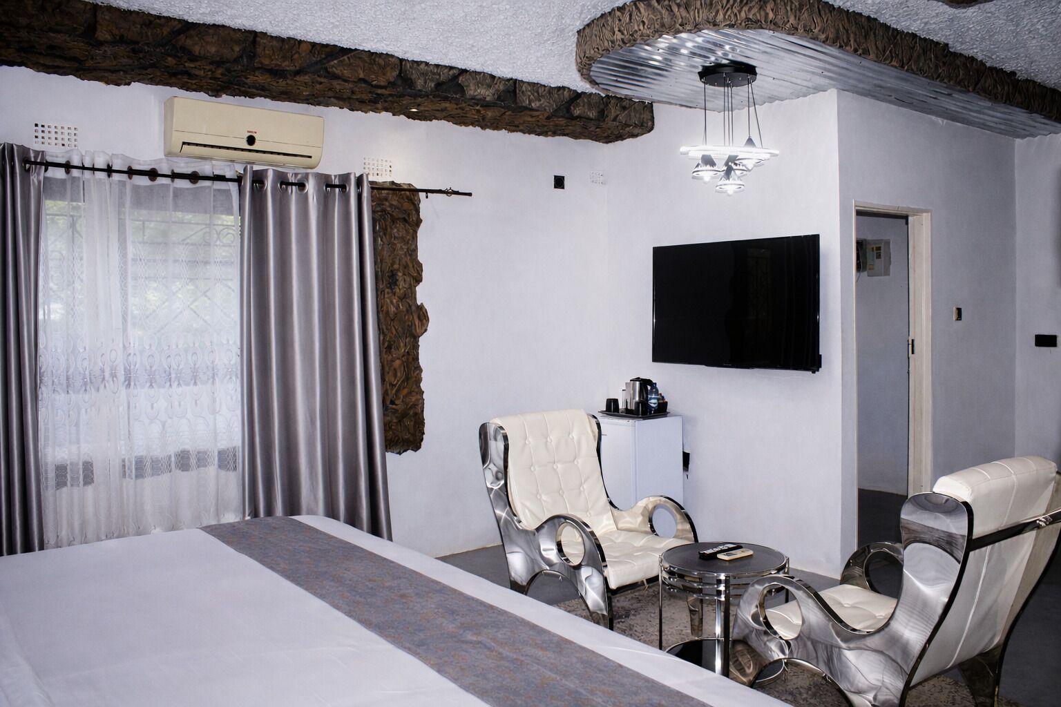 A hotel room with a large bed, two armchairs, a small table, a TV, and a stone accent wall.