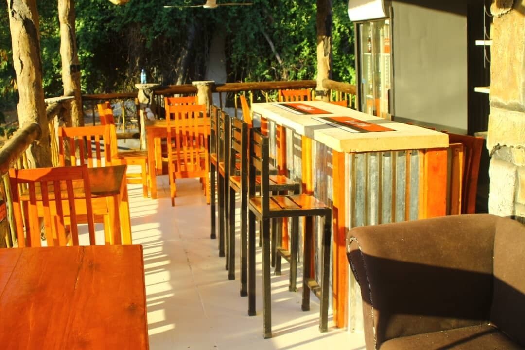 An outdoor seating area with wooden tables and chairs, surrounded by trees.