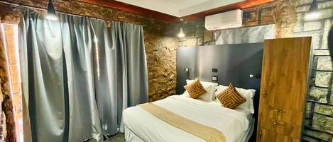 Un dormitorio con cama, cortinas, cabecero, armario de madera y pared de piedra.