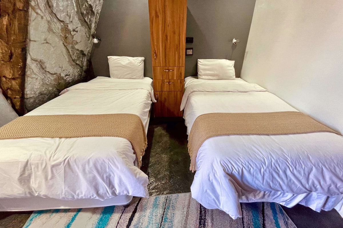 A room with two beds, a wooden wardrobe, and a marble wall.