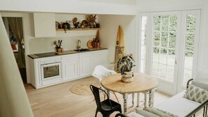 A kitchen with white cabinets, a black countertop, and a surfboard leaning against the wall. - Maison de Vacance en Lisière de Forêt (Labenne)