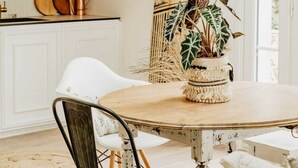 A dining area with a round table, chairs, a surfboard, and a potted plant. - Maison de Vacance en Lisière de Forêt (Labenne)