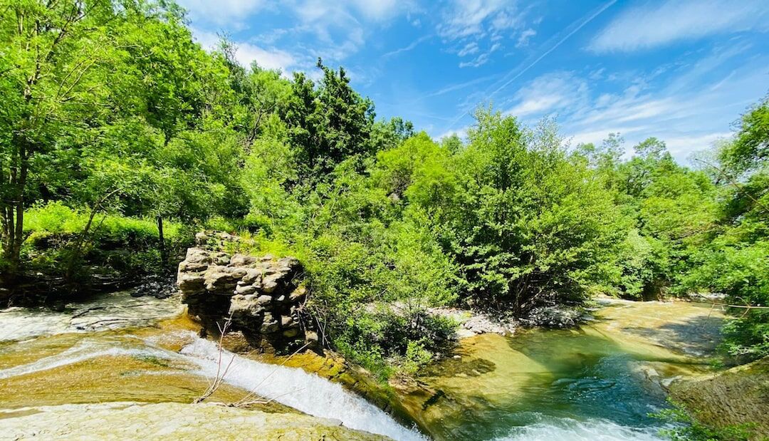 A natural landscape with a flowing river, dense greenery, and a rocky outcrop.