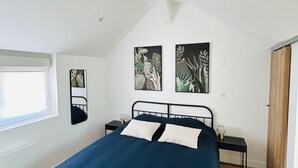 Un dormitorio con una cama, una ventana, una mesita de noche y dos cuadros colgados en la pared.
