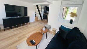 Una sala de estar moderna con un sofá negro, una mesa de centro de madera y un televisor. Una escalera conduce a un nivel superior.