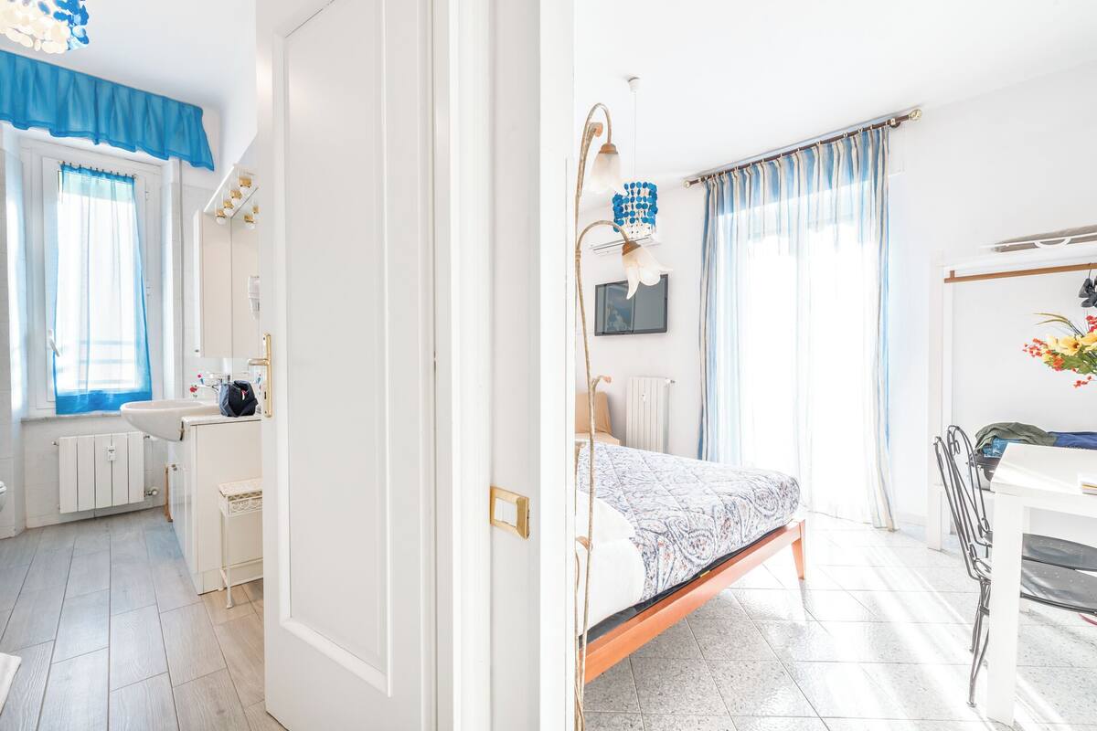 Een slaapkamer met een bed, een bureau, een stoel, een raam met gordijnen en een radiator.