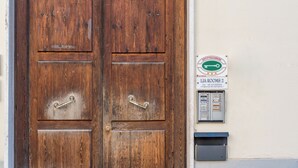 Une porte double en bois avec une poignée en métal, une enseigne indiquant « CHAMBRES LIA 2 » et mentionnant les coordonnées, ainsi qu’un coffret électrique fixé au mur.