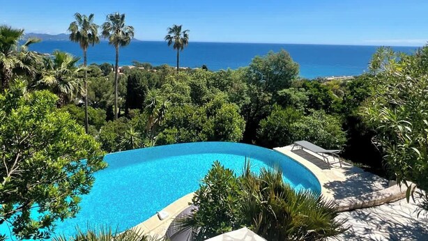 A clear blue swimming pool surrounded by lush greenery and palm trees, with a view of the ocean and distant mountains. - Top of Villa sea view,  heated swimming pool (Roquebrune-sur-Argens)