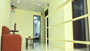 A hotel corridor with a red chair, a small table, a fire extinguisher, and a door with a metal frame. - Siamese Serenity Stays (Pattaya)