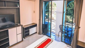 A hotel room with a bed, a TV, a desk, and a balcony with a table and chairs. - Siamese Serenity Stays (Pattaya)