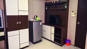 A compact kitchen with a built-in refrigerator, a microwave, and a small sink. There is a television on a wooden shelf above the counter. - Siamese Serenity Stays (Pattaya)