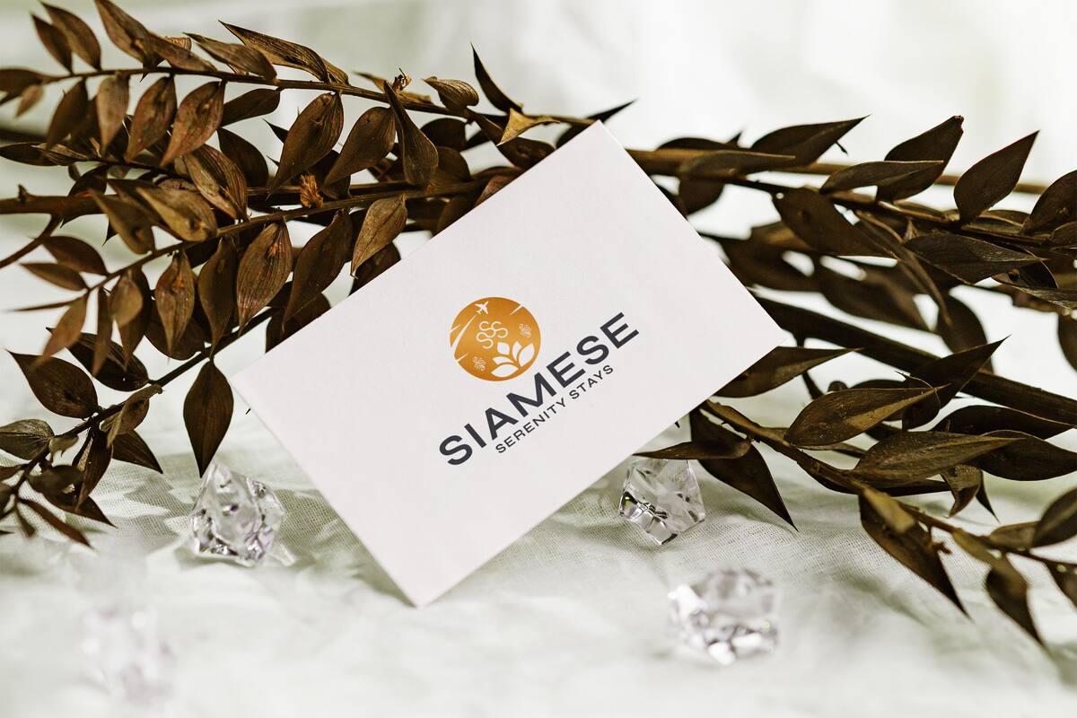 A business card with the text "SIAMESE" and "SERENITY STAYS" against a white background, surrounded by dried leaves and clear crystals.