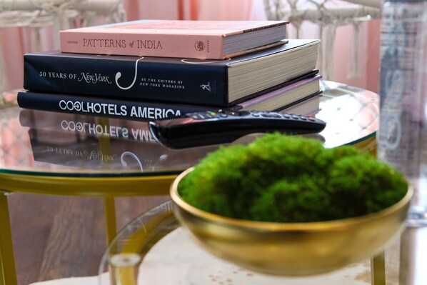 A stack of books on a glass table, a remote control, and a bowl of green moss.