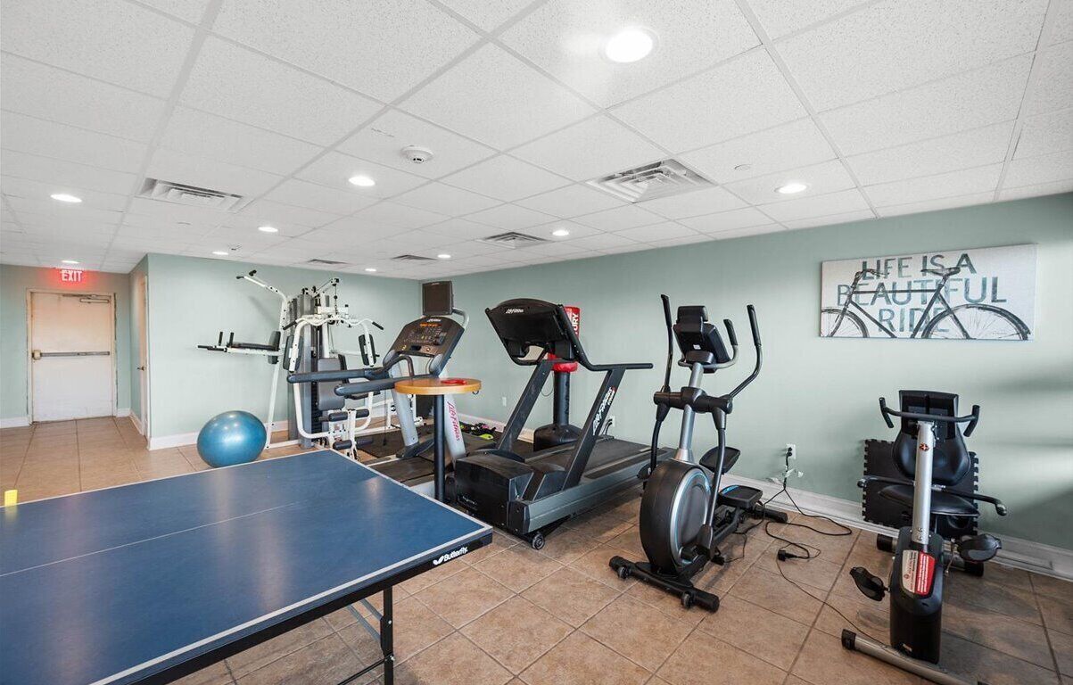 Un gimnasio con equipo de ejercicio, una mesa de ping pong y decoración de pared motivacional.