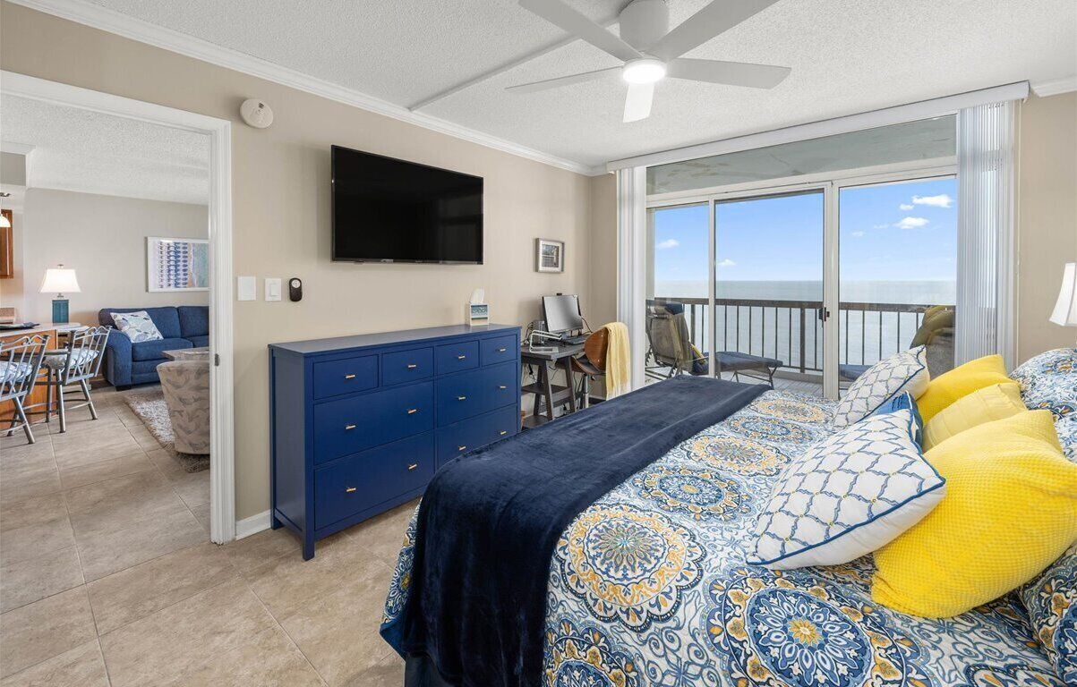 Ein Schlafzimmer mit Bett, Kommode, Fernseher und einem Balkon mit Blick.