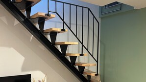 A modern staircase with wooden steps and black railings, a flat-screen TV on a wooden console, and a vase with dried flowers. - Little House built in 2024 and very comfortable. Near Annecy (Cuvat)