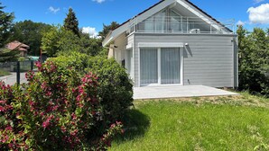 A modern two-story house with a large sliding glass door, surrounded by lush greenery and a well-maintained lawn. - Little House built in 2024 and very comfortable. Near Annecy (Cuvat)