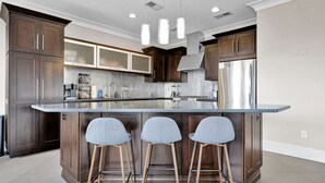 Una cocina moderna con armarios de madera oscura, una isla grande con taburetes de bar, electrodomésticos de acero inoxidable e iluminación colgante.