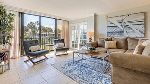 A spacious living room with a large window, a sofa, a chair, and a coffee table. - Luxe Fort Pierce Beach Condo w/ Golf Views! (Fort Pierce)