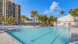 A swimming pool with blue lounge chairs and palm trees, surrounded by a hotel building. - Luxe Fort Pierce Beach Condo w/ Golf Views! (Fort Pierce)