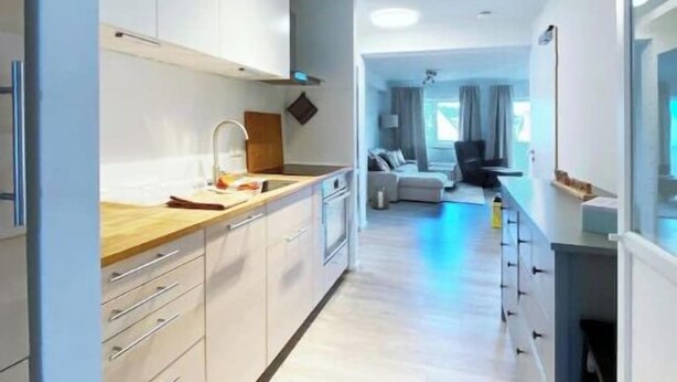 Una cocina moderna con armarios blancos, encimera de madera y vistas al área de estar, que incluye un sofá y cortinas.