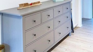 Un aparador gris con varios cajones, un juguete de madera pequeño encima y una caja blanca.