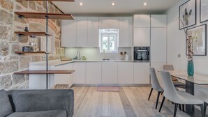 A modern kitchen with white cabinets, a stone wall, and a dining area with a gray sofa and chairs. - Funky Donkey (Split)