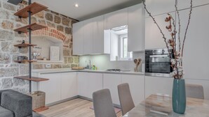 A modern kitchen with white cabinets, a stone accent wall, a built-in oven, and a dining area with a marble table and chairs. - Funky Donkey (Split)