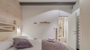 A modern bedroom with a bed, a wooden headboard, a small shelf, and a door leading to another room. - Funky Donkey (Split)