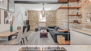 A modern living room with a stone wall, a sofa, a dining table, and a kitchen area with wooden shelves. - Funky Donkey (Split)