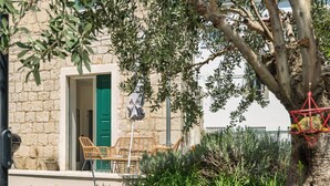 A stone building with a green door, wicker furniture, and a tree in the foreground. - Funky Donkey (Split)