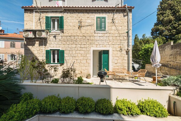 A stone building with green shutters, a barbecue grill, and outdoor seating.