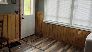 Ein Zimmer mit Holztür, einem Fenster mit Jalousien, einer Holzbank und einer Heizung.