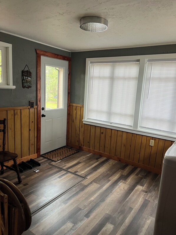 Une pièce avec une porte en bois, une fenêtre avec des stores, un banc en bois et un radiateur.