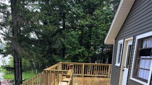 Eine Holzterrasse mit einer Holztreppe, die zu einem weiteren Terrassenbereich führt, umgeben von Bäumen und einem Haus mit weißer Tür und Fenstern.