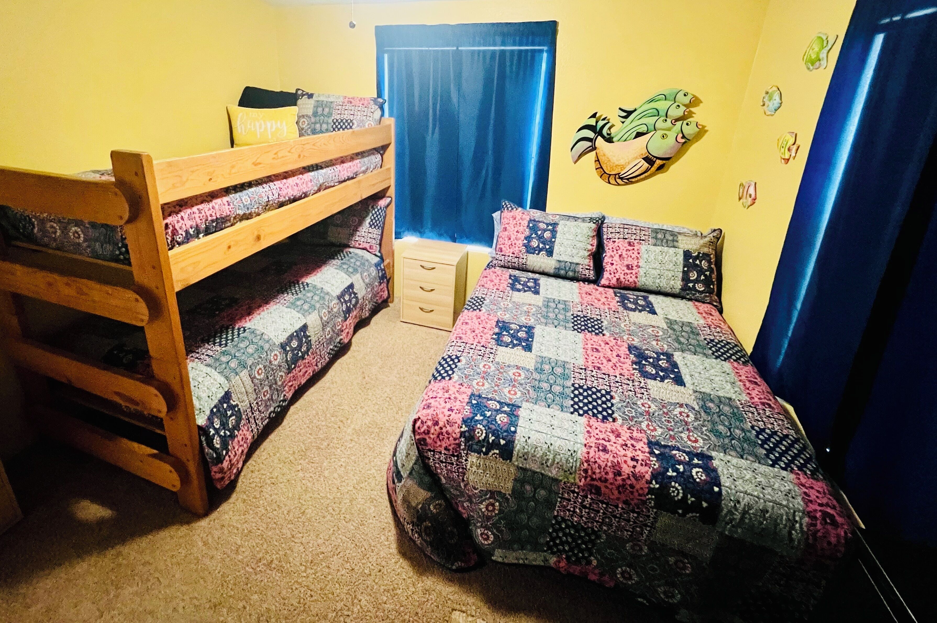 A dormitory room with bunk beds, a quilted bed, a small desk, and a wall decal.