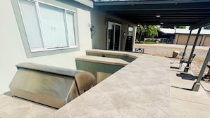 An outdoor kitchen area with a countertop and grill, a covered seating area, and a pool in the background. - The perfect spot for family & friend! Best private getaway in Mohave Valley 🔆 (Mohave Valley)