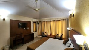 Quarto de hotel com cama, escrivaninha, cadeira, televisão e ar condicionado.