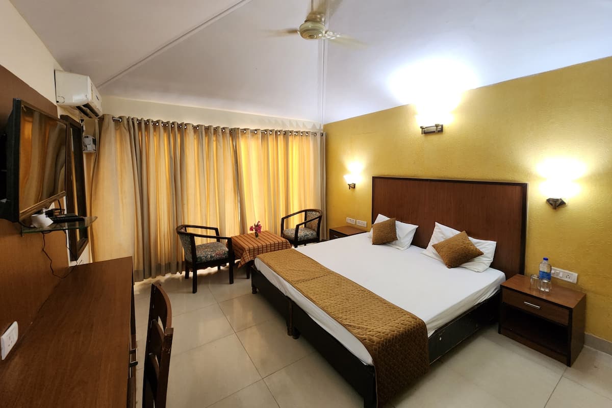 A hotel room with a bed, bedside tables, a desk with a chair, a ceiling fan, and curtains.