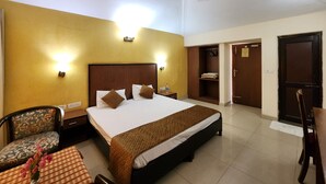 Quarto de hotel com uma cama, mesas de cabeceira, uma cadeira, uma mesa com um vaso, um guarda-roupa e uma porta.