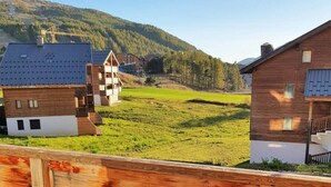 A wooden deck with red chairs overlooking a green field and buildings. - 1st floor, view mountain, swimming pool, parking, tv, ski locker, 32m², La Joue du Loup (Agnières-en-Dévoluy)