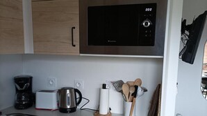 A modern kitchen with wooden cabinets, a stainless steel microwave, a kettle, a toaster, and a coffee maker. - 1st floor, view mountain, swimming pool, parking, tv, ski locker, 32m², La Joue du Loup (Agnières-en-Dévoluy)