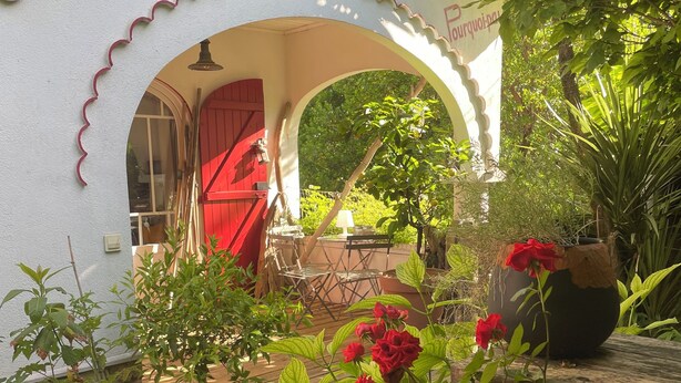 Un espacio al aire libre con patio, terraza de madera, plantas en macetas y una puerta roja.