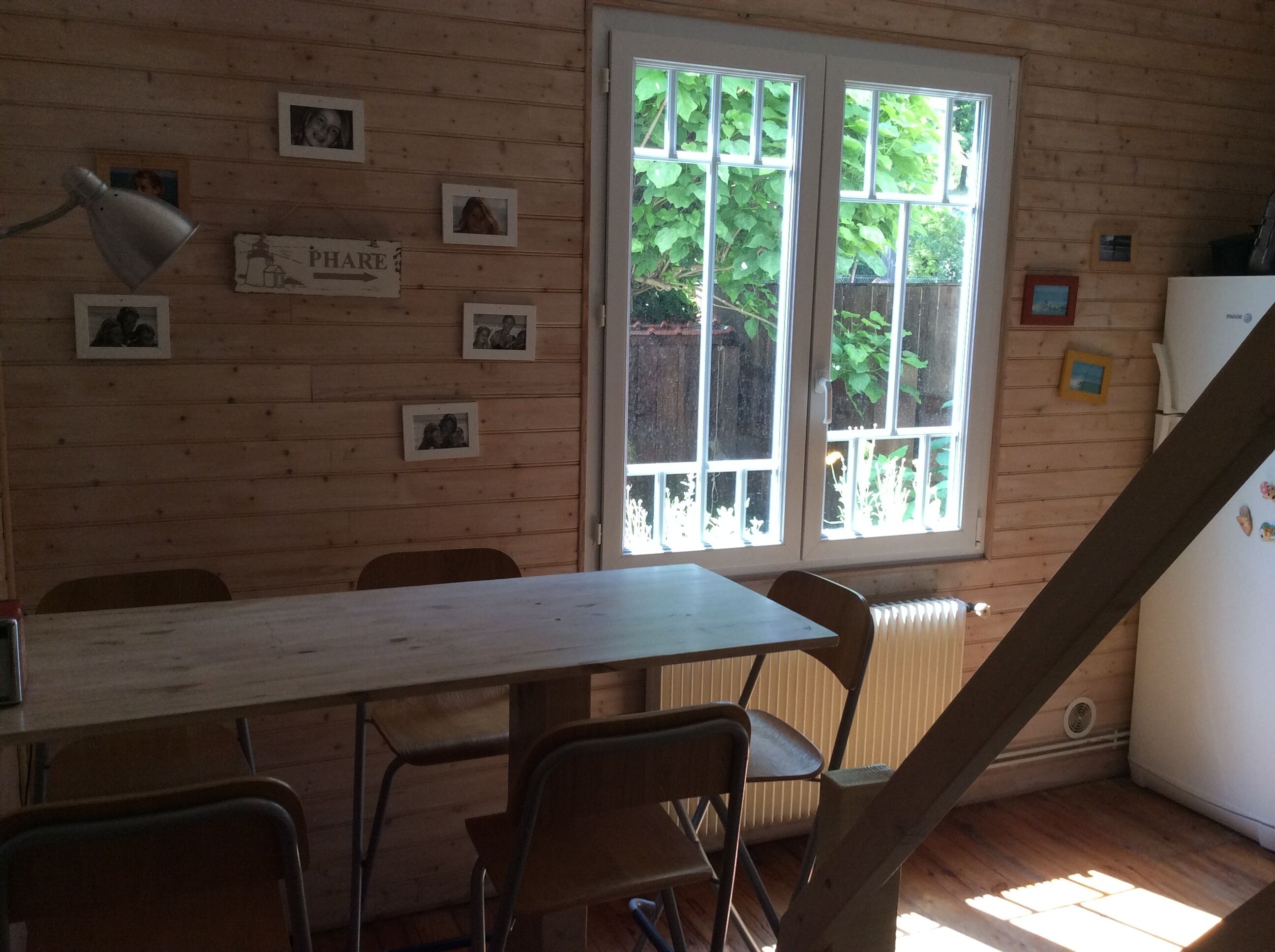 Uma área de refeições com mesa e cadeiras, uma janela com vista para o verde, e um refrigerador no canto.