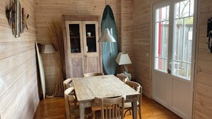 Un interior de madera con una mesa de comedor, sillas, una tabla de surf y una lámpara.