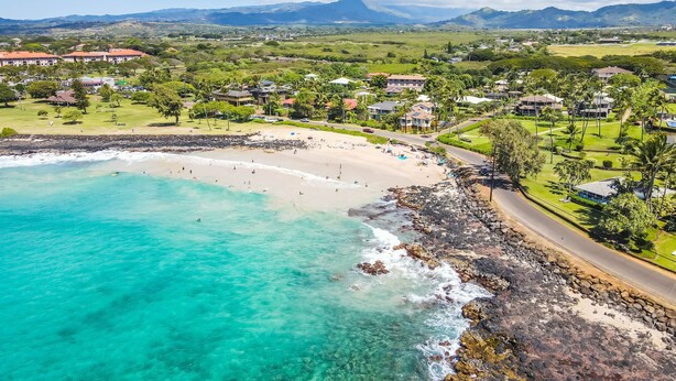Un pueblo costero con una playa, casas y montañas al fondo.