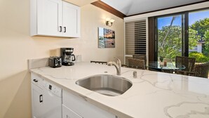 Una cocina moderna con armarios blancos, un lavamanos de acero inoxidable y una cafetera.