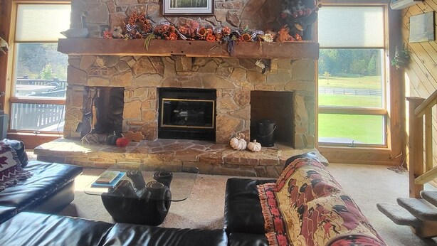 A cozy living room with a stone fireplace, leather sofa, and large windows. - Beautiful Lodge for Weddings, Reunions, Events or Family Gatherings. Sleeps 25+ (Redfield)
